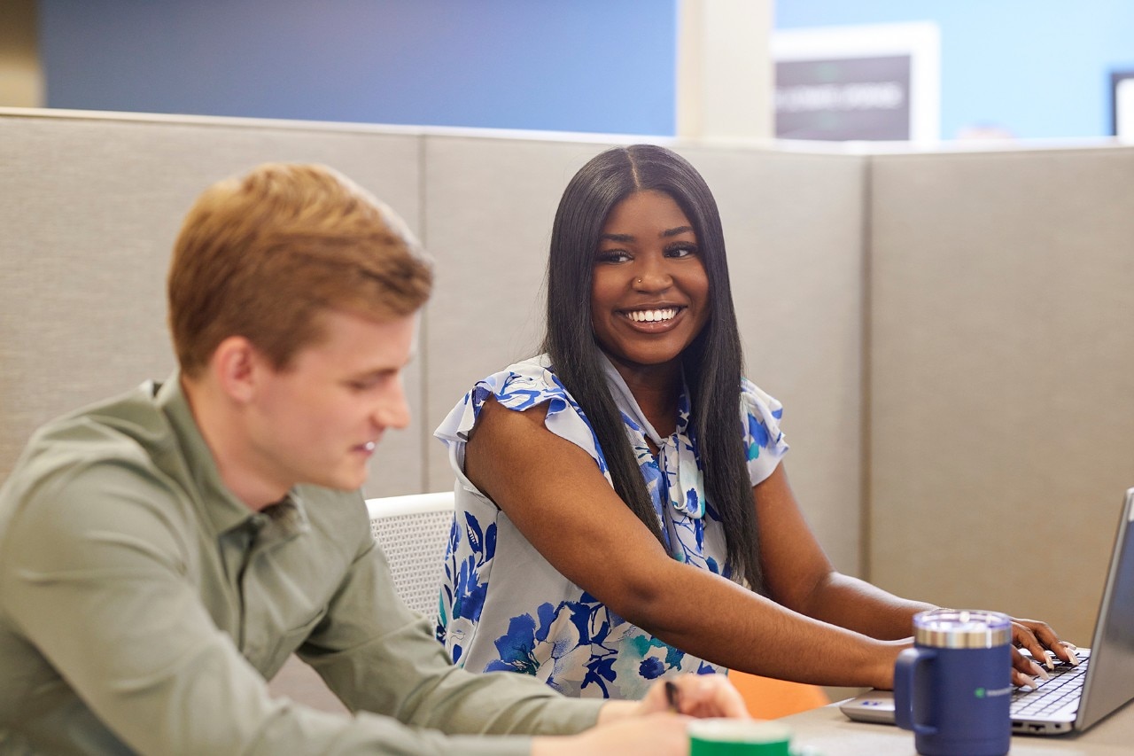 Two Enterprise Mobility team members discussing a document on a laptop computer while sitting in an office booth.   
