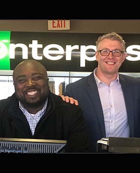 Two employees in front of Enterprise sign