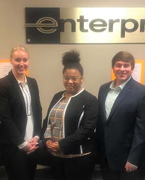 Three employees in front of Enterprise sign