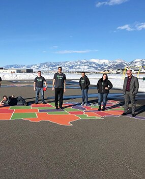 Employees standing on painting of the United States on parking lot in front of mountains