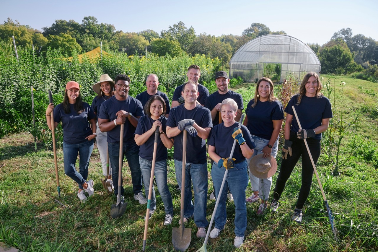 A group of smiling Enterprise Mobility team members holding shovels and rakes standing in a sunny field