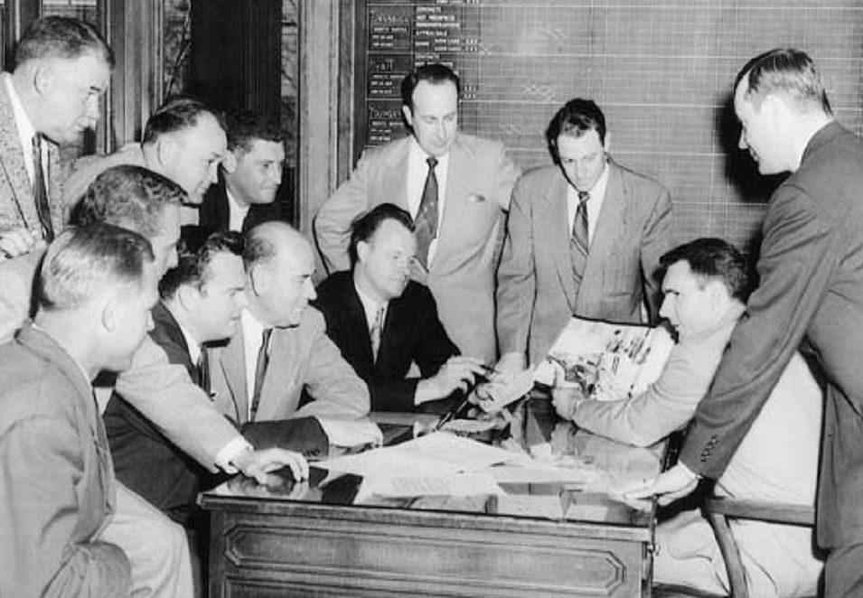 Black and white photo of Jack Taylor, founder and former CEO, and other men discussing business.