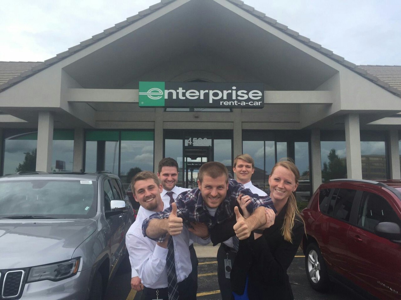 Four Enterprise interns holding up a fifth intern in front of Enterprise Rent-a-Car building