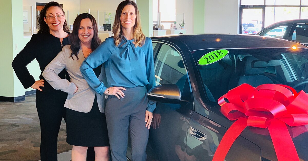 Three Female Enterprise employees standing next to a car with a red ribbon on it