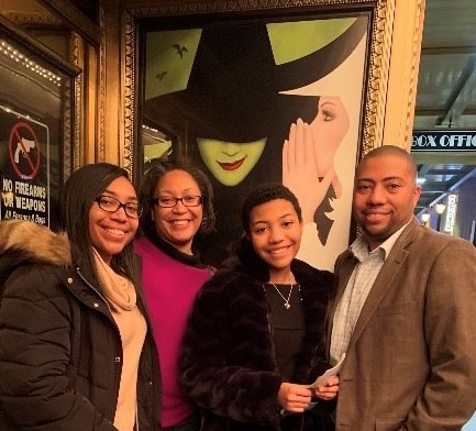 Jason B. with his family in front of a poster for the musical Wicked
