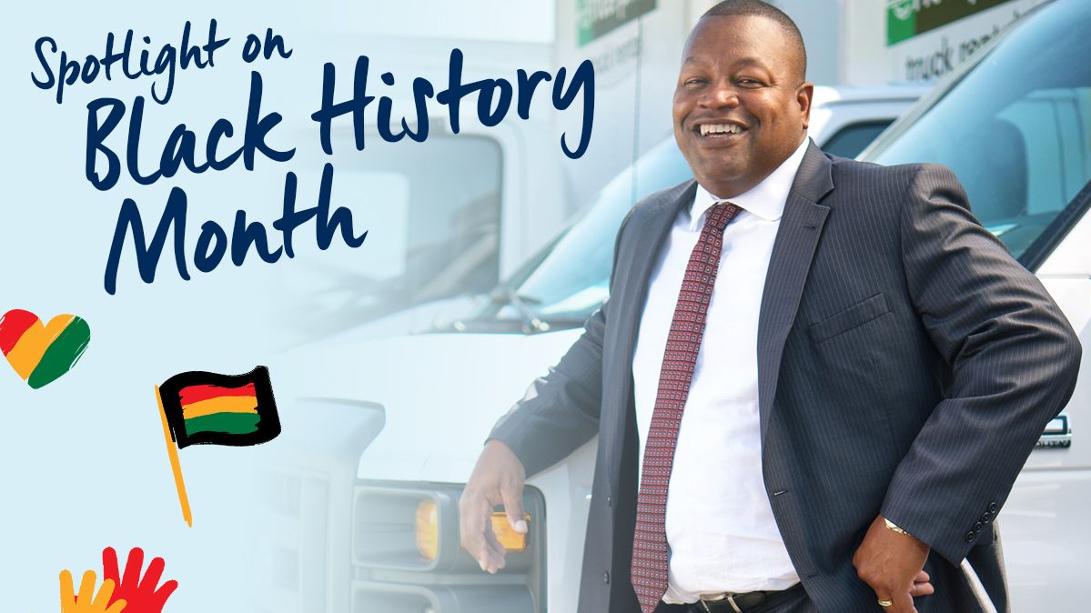 Kevin in a suit leaning up against an Enterprise Rental Truck with Black History Month Icons