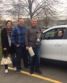 Three employees standing next to a car with someone in the driver's seat