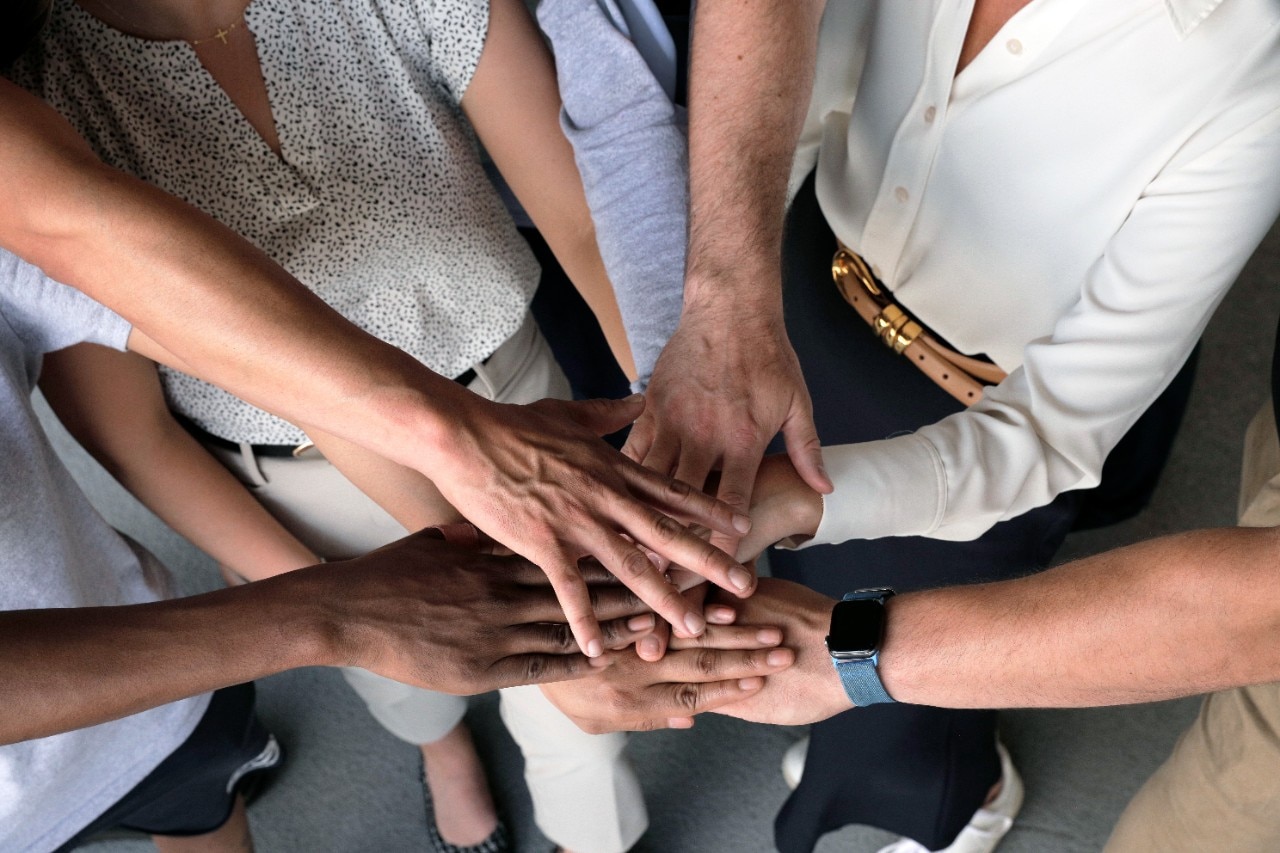 Team members put stack hands on top of each other in huddle