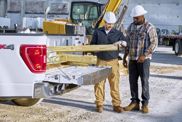 Deux hommes portant des casques de sécurité sur un chantier de construction, retirant du bois de l’arrière d’une camionnette.